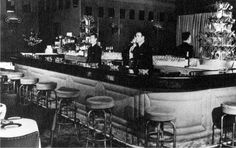 an old black and white photo of a bar with stools in front of it