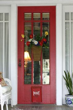 a red front door with a basket full of flowers on it and a lamp next to it