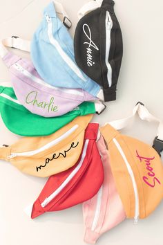 five fanny bags with names on them sitting next to each other, all in different colors