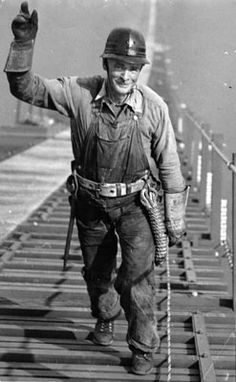 a black and white photo of a man walking across a bridge with his hand in the air