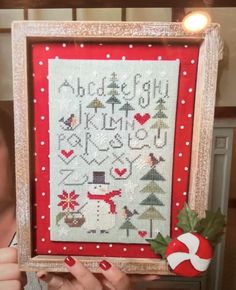 a woman holding up a framed cross stitch sample