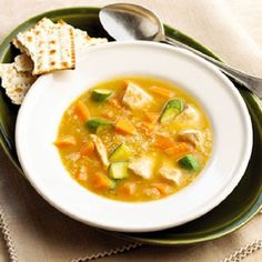 a white bowl filled with soup next to crackers on top of a green plate