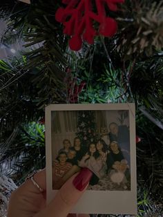 a woman holding up an old photo in front of a christmas tree with red decorations