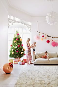 two children standing in front of a christmas tree with decorations on the wall behind them