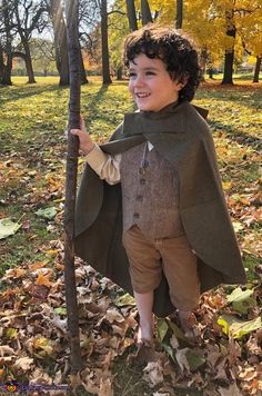 a young boy dressed in a costume standing next to a tree with leaves on it