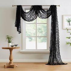 a black sheer curtain hanging from a window next to a table with potted plants