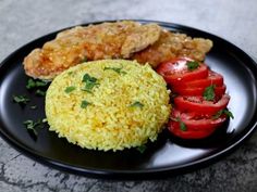 a black plate topped with rice, tomatoes and fried chicken next to two slices of tomato