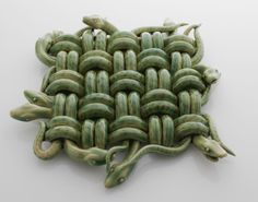 a green woven object on a white surface with two snakes crawling around it's sides