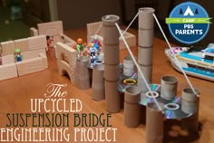 the unfinished suspension bridge engineering project is displayed on a table with toys and paper rolls