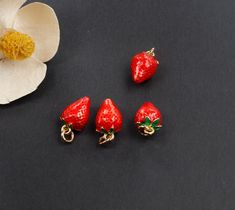 three red strawberry charms sitting next to a white flower on a black surface with the petals still attached