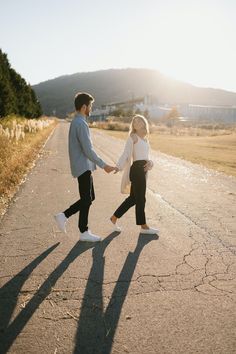 a man and woman holding hands while walking down the road