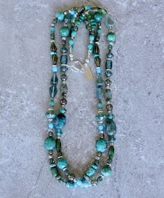 This terrific 2-Strand Necklace displays an impressive number of Turquoise and Czech Glass elements, paired with Sterling Silver. There are 33 discrete components in the design, in a multitude of blue, green and silver hues. A veritable treasure trove of styles. While the 33 styles are too many to elucidate, some notable elements include: Striking Czech Faceted Saucers in appealing Picasso turquoise hues Classic blue Turquoise Ovals with distinctive dark brown matrix Glossy light and dark green Turquoise Rounds Striking translucent green Czech Glass Teardrops with metallic gold stripes Rich turquoise-blue long Barrel Beads Eye-catching translucent aqua Czech Glass Pyramids Elegant Jade swirl Czech Glass Cylinders Shining Sterling Silver Discs and Stamped Rounds & Rondelles Uncommon aqua-ta Necklace Displays, Gold Stripes, Green Peridot, Toggle Clasp, White Heart, Green Turquoise, Tube Beads, Classic Blue, Heart Beads