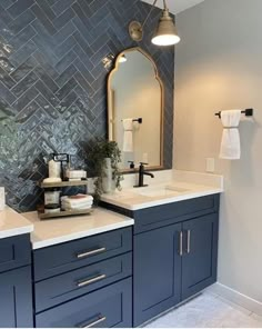 a bathroom with blue cabinets and white counter tops in front of a gray tiled wall