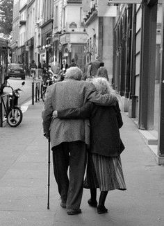 an old man and woman walking down the street with their backs to each other,