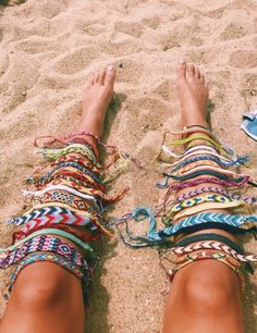 a woman's feet in sandals on the beach with colorful bracelets around her ankles