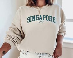 ✨Basic Info✨ This listing is for a sweatshirt that says 'SINGAPORE 1965' on the front! The color of the sweatshirt is 'Sand', but contact me if you would like to see a different color! I also offer sweatshirts with other cities, but let me know if there is a city you don't see that you would like me to make! Make sure you check out our other great products like our Potions Collection T-Shirts :) ✨Shirt and Sizing Info✨ All VillainessLabs crewneck sweatshirts are printed on a Gildan 18000 Unisex Cream Crew Neck Sweatshirt With Letter Print, Beige Letter Print Sweatshirt For Loungewear, Cream Letter Print Sweatshirt For Loungewear, University Crewneck, City Sweatshirt, Crew Neck Sweatshirt Sand, Souvenir Sweatshirt, Georgetown Sweatshirt, University Sweatshirts