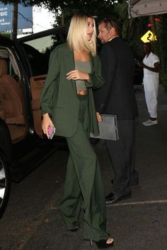 the blonde woman is walking down the street with her hand on her hip while wearing a green suit