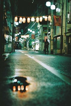 an empty city street at night with lights strung above it and people walking on the sidewalk