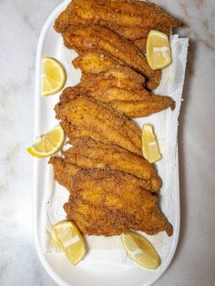 fried fish with lemon wedges on a white plate