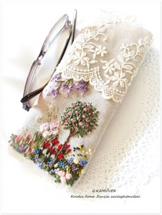 a pair of glasses sitting on top of a piece of cloth covered in embroidered flowers