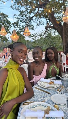 three women sitting at a table with plates and silverware in front of them, smiling for the camera