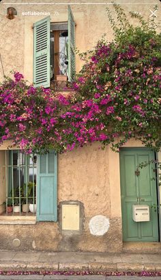 an old building with green shutters and pink flowers