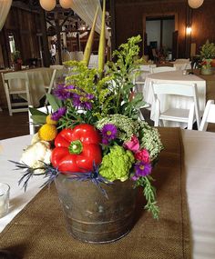 an arrangement of flowers and vegetables in a bucket on a table at a wedding reception