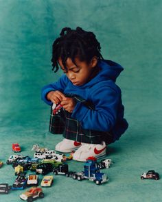 a young child playing with toy cars on the floor in front of a blue background