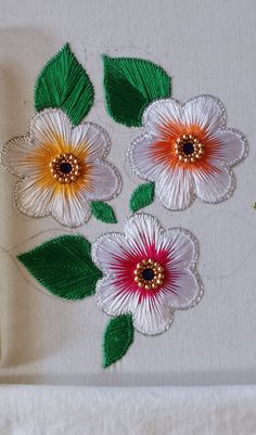 three flowers on a white table cloth with green leaves and beads in the middle one is red, yellow and white