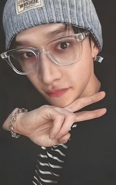 a young man wearing glasses and a beanie pointing to the side with his finger