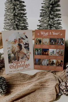 two christmas cards sitting on top of a table next to pine cones and fir trees