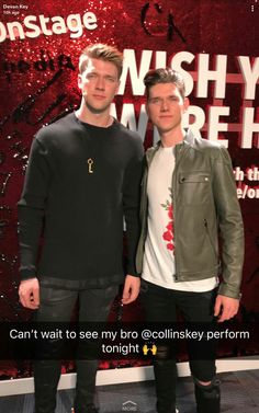 two men standing next to each other in front of a red wall with words on it