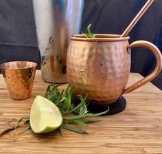 two copper mugs sitting on top of a wooden table next to a lime slice