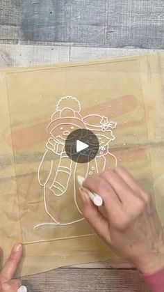 someone is drawing on some paper with their hand and thumbnails, while another person's hands are holding something in front of them