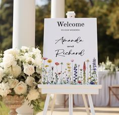 a welcome sign sitting on top of a easel next to a bouquet of flowers