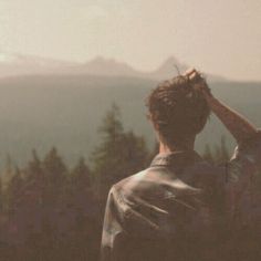 a man standing on top of a lush green hillside next to a forest filled with trees