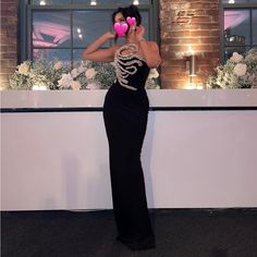 a woman in a long black dress holding a heart shaped object up to her face