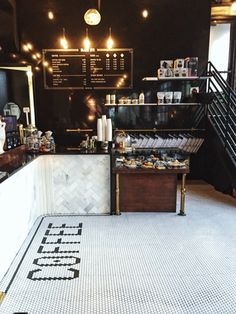 the inside of a coffee shop with white tile flooring and black walls, along with stairs