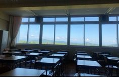 an empty classroom with many desks and windows overlooking the mountain range in the distance