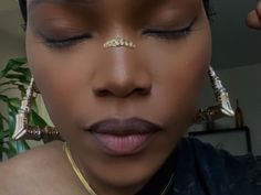 a close up of a person wearing gold jewelry and piercings on her nose with a plant in the background