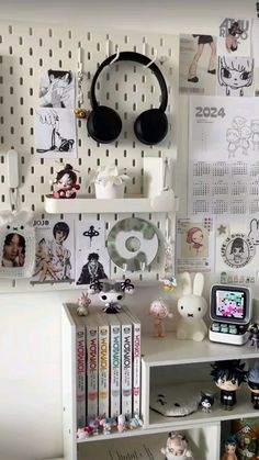 a white desk topped with lots of books and headphones next to a wall covered in pictures