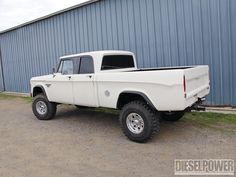 an old white truck parked in front of a blue metal building on the side of a road