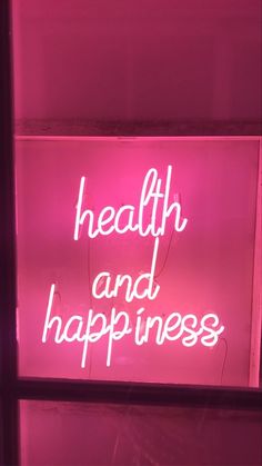 a neon sign that says health and happiness in white letters on a pink wall behind it