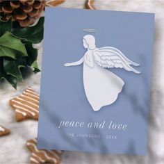 a christmas card with an angel on it next to some cookies and holly leaves in the background