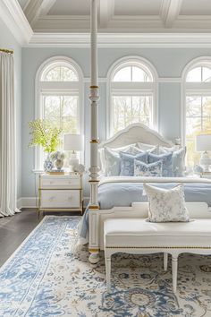 a bedroom with blue walls and white furniture in the center, along with large windows