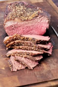 sliced meat sitting on top of a wooden cutting board next to a knife and fork