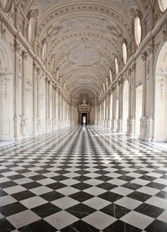 an empty hallway with black and white checkered flooring on one side and columns on the other