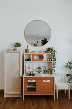 a small wooden play kitchen with an oval mirror on the wall and potted plants next to it