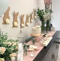 a table topped with cakes and flowers next to bunnies hanging on the wall behind it