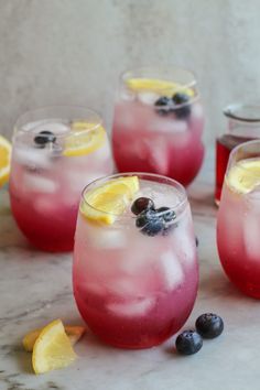 three glasses filled with blueberries and lemonade on top of a marble countertop